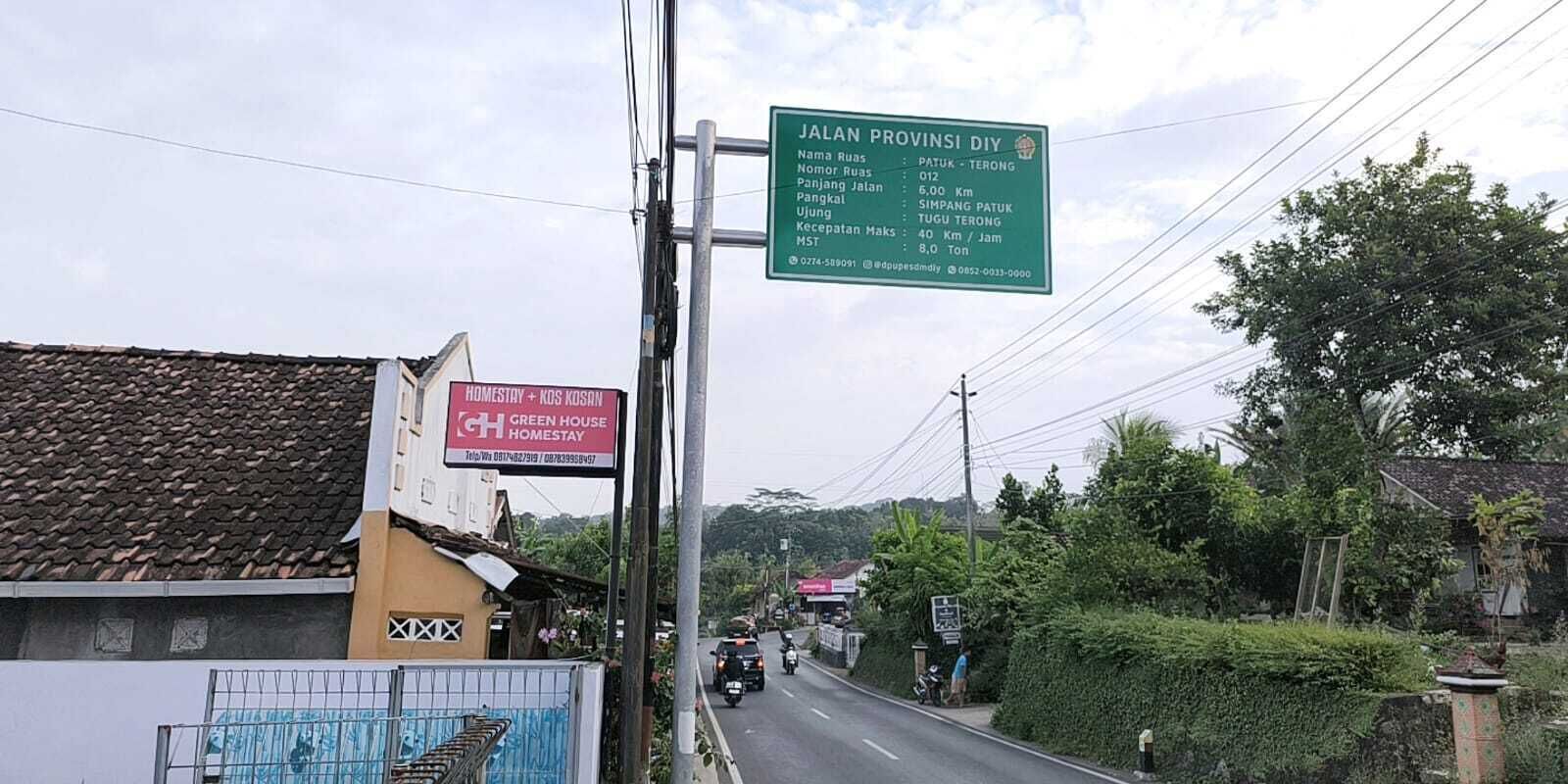 A road with a green signboard listing local destinations and distances.