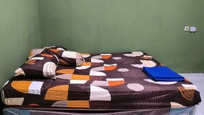 Ein Bett mit gemustertem Überwurf und Kissen, eine blaue Ordner und eine weiße Steckdose.
