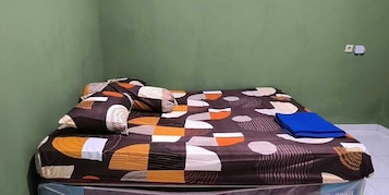 Uma cama com colcha estampada e almofadas, uma pasta azul e uma tomada de parede branca.