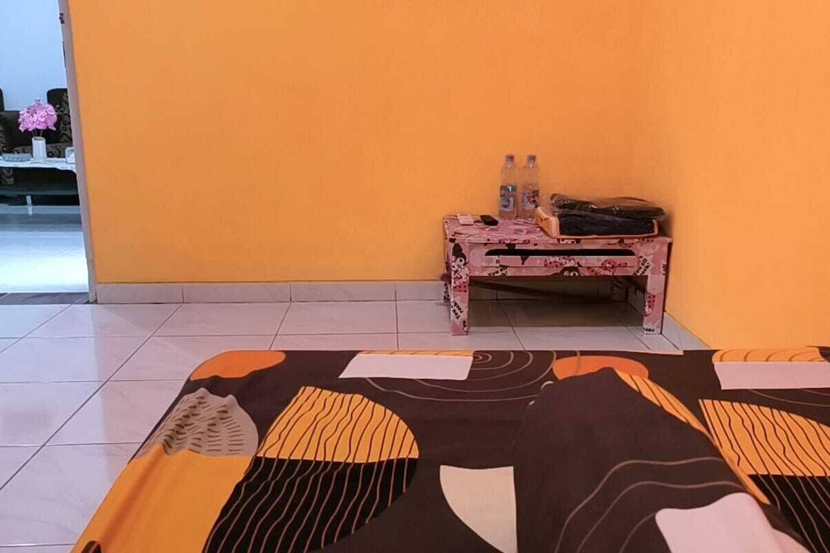 A room with a bed, a small table with a pink patterned tablecloth, and a sofa with a floral cushion.