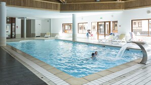 An indoor swimming pool with a wooden ceiling, tiled walls, and lounge chairs around the pool. - Résidence Odalys L'orée des Pistes (Saint-Sorlin-d'Arves)