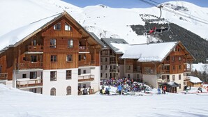A wooden lodge with multiple balconies, a ski lift, and a crowd of people. - Résidence Odalys L'orée des Pistes (Saint-Sorlin-d'Arves)