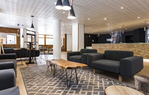 A modern lounge area with sofas, a coffee table, pendant lighting, and a reception desk.