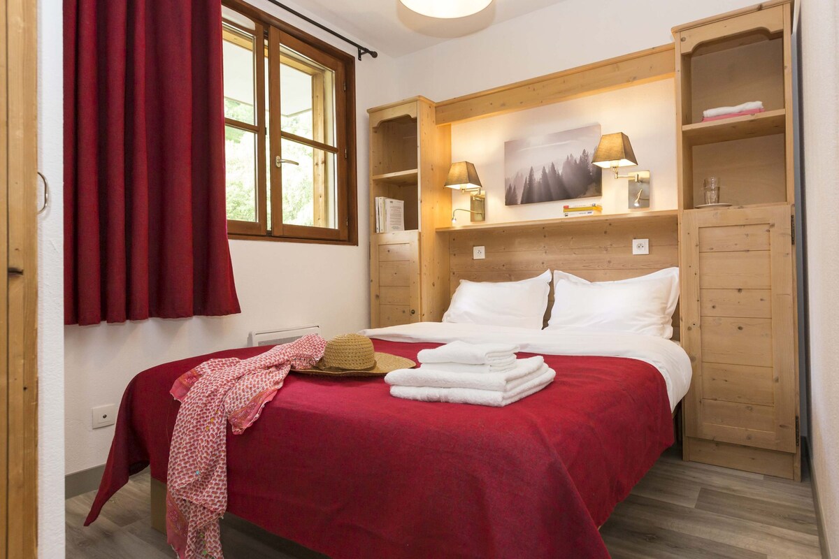Ein Schlafzimmer mit einem Bett, einem Holzschrank, einem Fenster mit Vorhängen und einer Wandlampe.