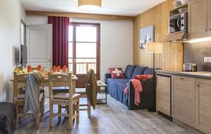 A cozy room with a wooden dining table, chairs, a sofa, and a kitchen area with cabinets and appliances.