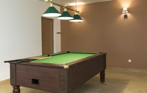 A pool table with three green overhead lamps, a door, and a wall socket.