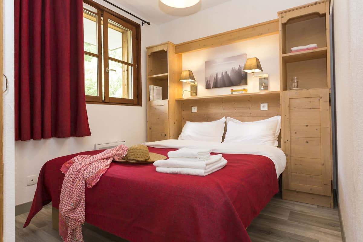 Une chambre à coucher avec un lit, une armoire en bois, une fenêtre avec des rideaux et une lampe fixée au mur.