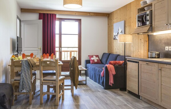 A cozy room with a wooden dining table, chairs, a sofa, and a kitchen area with cabinets and appliances.