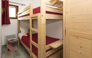 Une chambre avec un lit superposé, une fenêtre, une petite table avec un livre et un rideau rouge.
