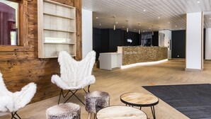 A modern interior with wooden walls, a reception desk, and a seating area with fluffy chairs and ottomans. - Résidence Odalys L'orée des Pistes (Saint-Sorlin-d'Arves)