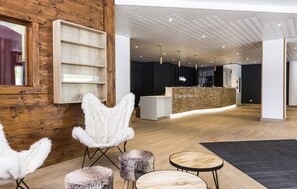 Ein modernes Interieur mit Holzwänden, einer Rezeption und einer Sitzecke mit weichen Sesseln und Poufs.