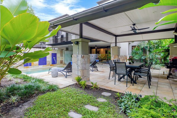A covered patio area with a pool, lounge chairs, and a dining table.