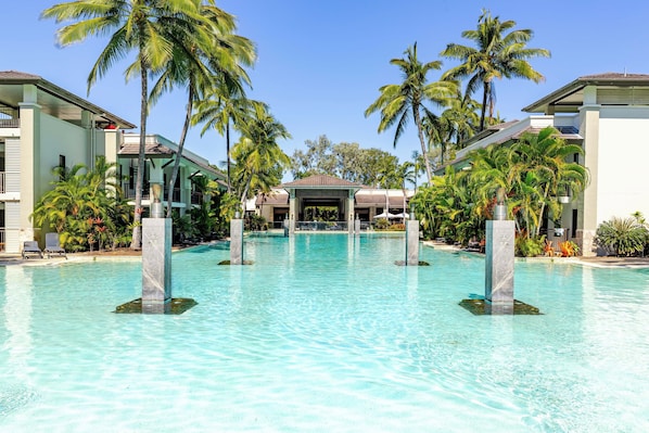 A pool area with clear water, palm trees, and a covered pavilion.