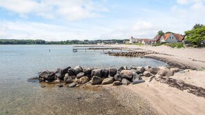 Vista panorámica de un lago con un muelle que se adentra en aguas tranquilas, rodeado de una playa arenosa y edificios residenciales.