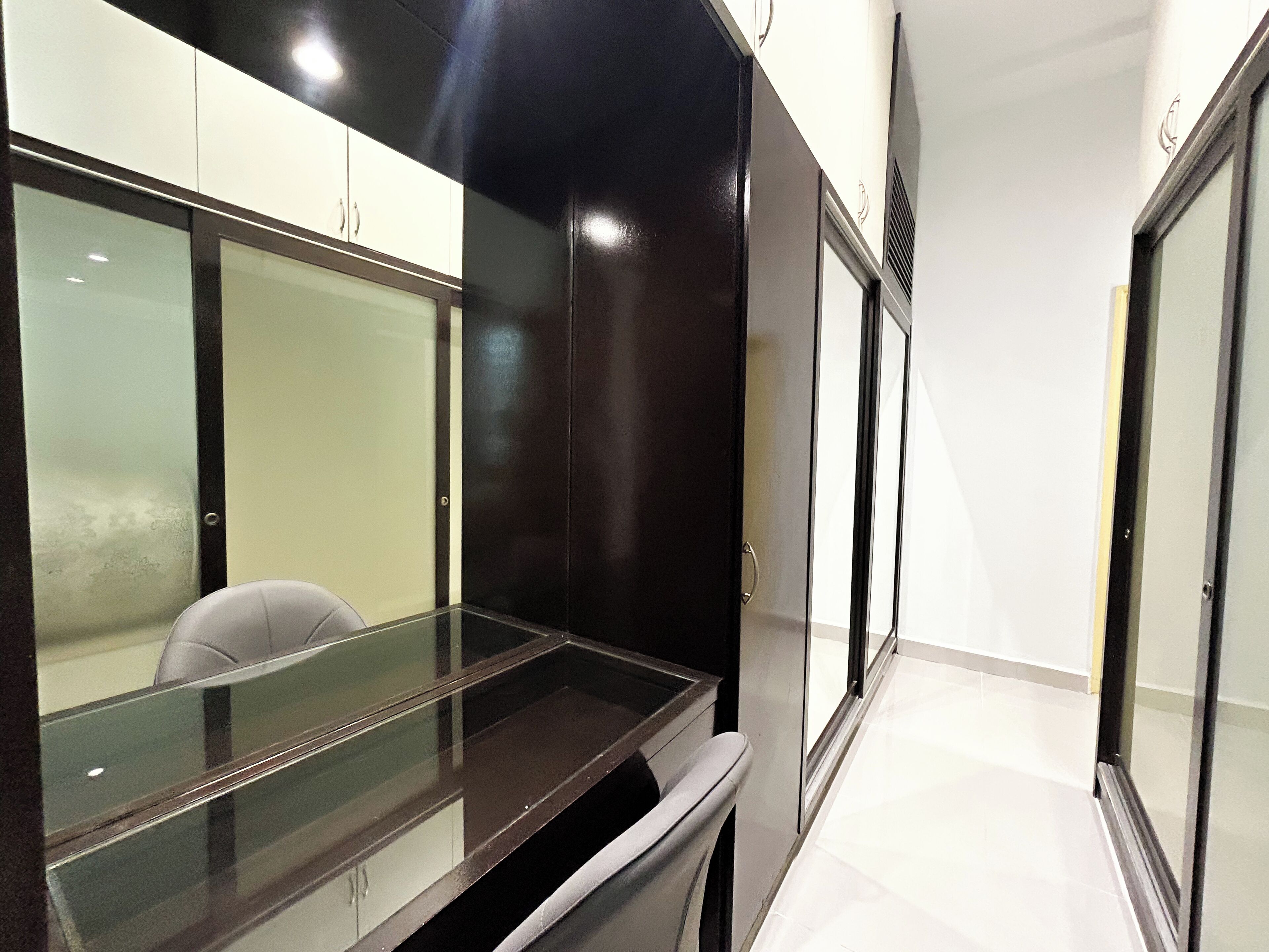 A modern office space with a glass desk, white cabinets, and a black accent wall.
