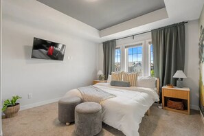 Ein Schlafzimmer mit einem Bett, zwei Nachttischen, einem an der Wand befestigten Fernseher und einem Fenster mit Vorhängen.