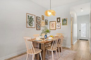 Ein Essbereich mit einem Holztisch, sechs Stühlen, einer Hängelampe und gerahmten Bildern an der Wand.