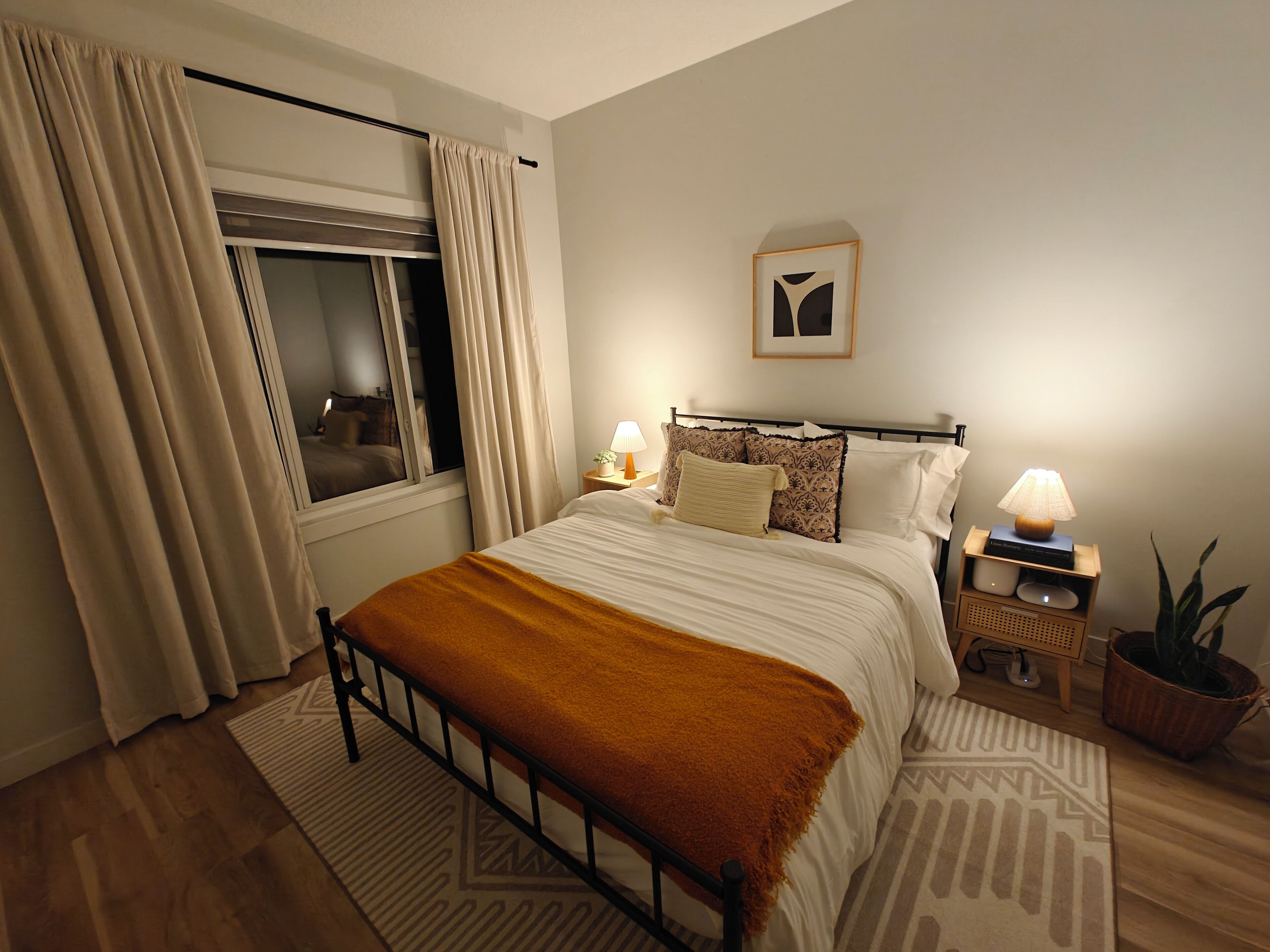 Een netjes ingerichte slaapkamer met een bed, nachtlampjes, een nachtkastje en een potplant.