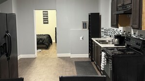 A modern kitchen with dark cabinetry, a stove, and a dining area with a table and chairs. - Spacious 2BR Full Kitchen Suite + Pool Table I
Patio + Private (Lawrenceville)