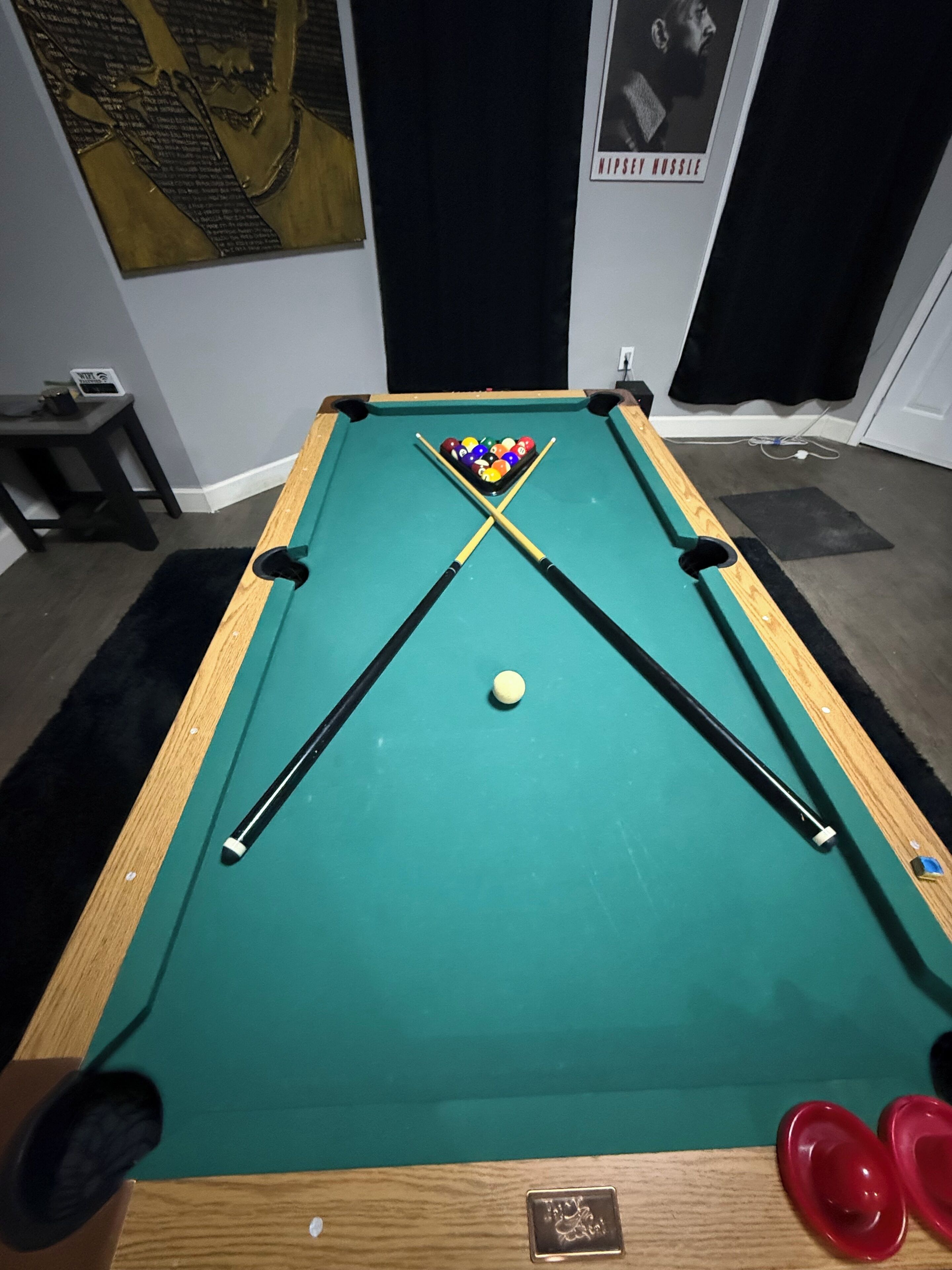 Une table de billard avec une boule blanche et un jeu de billes, une petite table avec un ordinateur portable et une tasse, et une affiche accrochée au mur.
