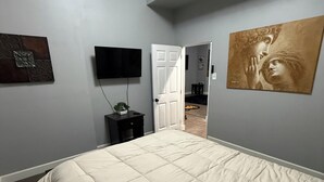 A bedroom with a large bed, a flat-screen TV mounted on the wall, a door leading to another room, and a painting on the wall. - Spacious 2BR Full Kitchen Suite + Pool Table I
Patio + Private (Lawrenceville)