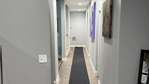 A hallway with a black carpet, grey walls, and a trash bin on the left. - Spacious 2BR Full Kitchen Suite + Pool Table I
Patio + Private (Lawrenceville)