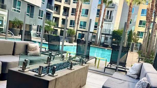 Un espace ext érieur moderne, aménagé avec des sièges, une table à plateau de verre, une piscine et une vue sur un immeuble à plusieurs étages doté de balcons.