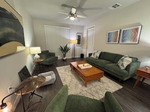 A living room with a ceiling fan, green sofas, a coffee table, and a lamp. - Charming 1-bedroom apartment in Irvine with pool, fitness room, close to shops. (Irvine)