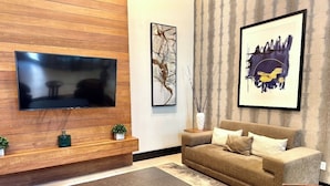 Un salon moderne avec un téléviseur à écran plat fixé à un mur en bois, un canapé marron avec des coussins, un pouf noir et deux tables d’appoint ornées d’objets décoratifs.
