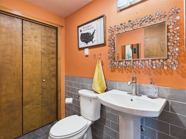 A bathroom with a wooden door, a toilet, a sink, and a mirror with a decorative frame.