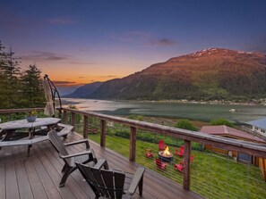 A deck with chairs and a table overlooking a lake and mountains.