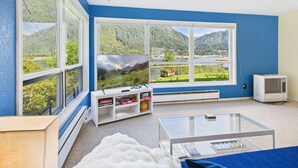A modern living room with large windows, a flat-screen TV, a white sofa, and a glass coffee table.