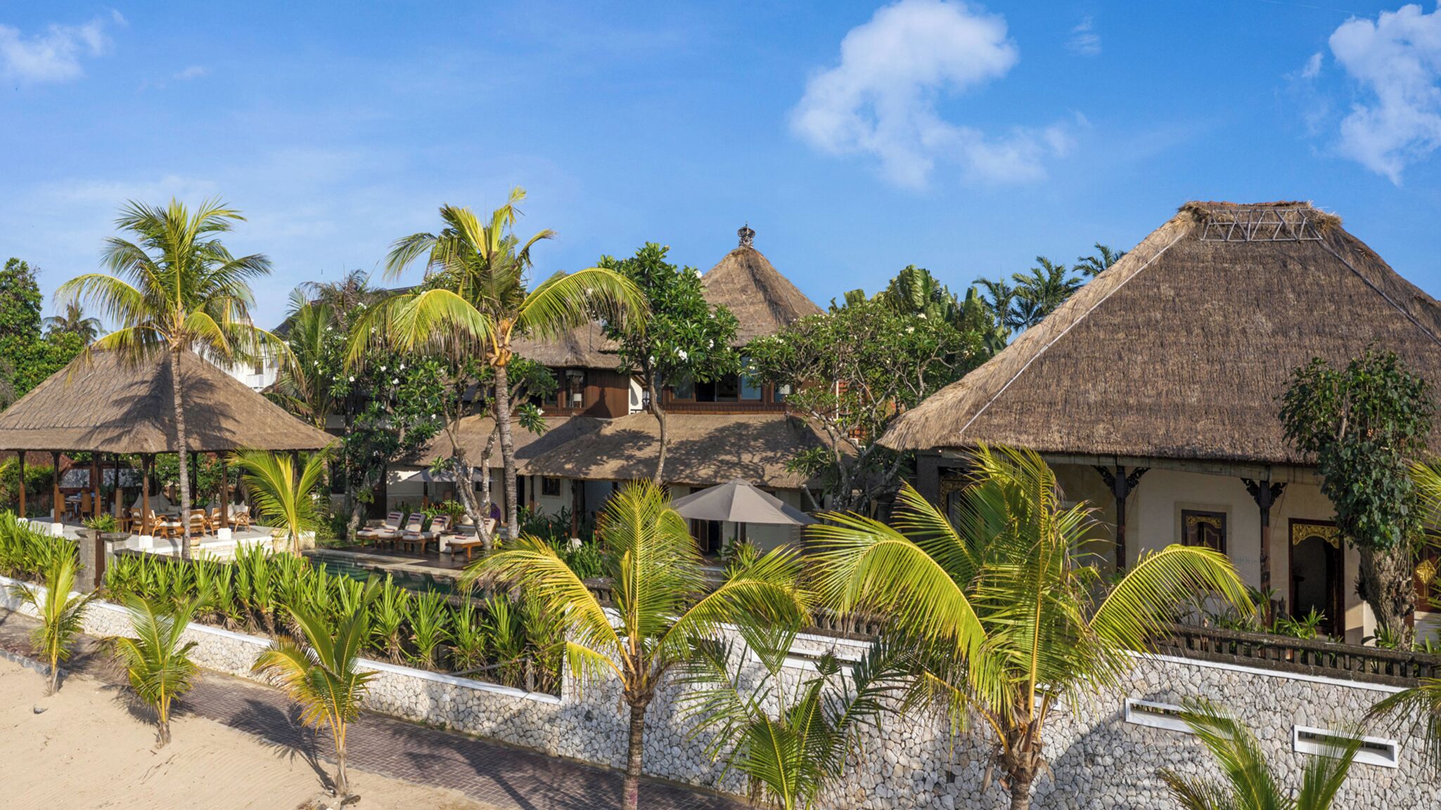 A resort with thatched-roof buildings, a pool area, and palm trees.