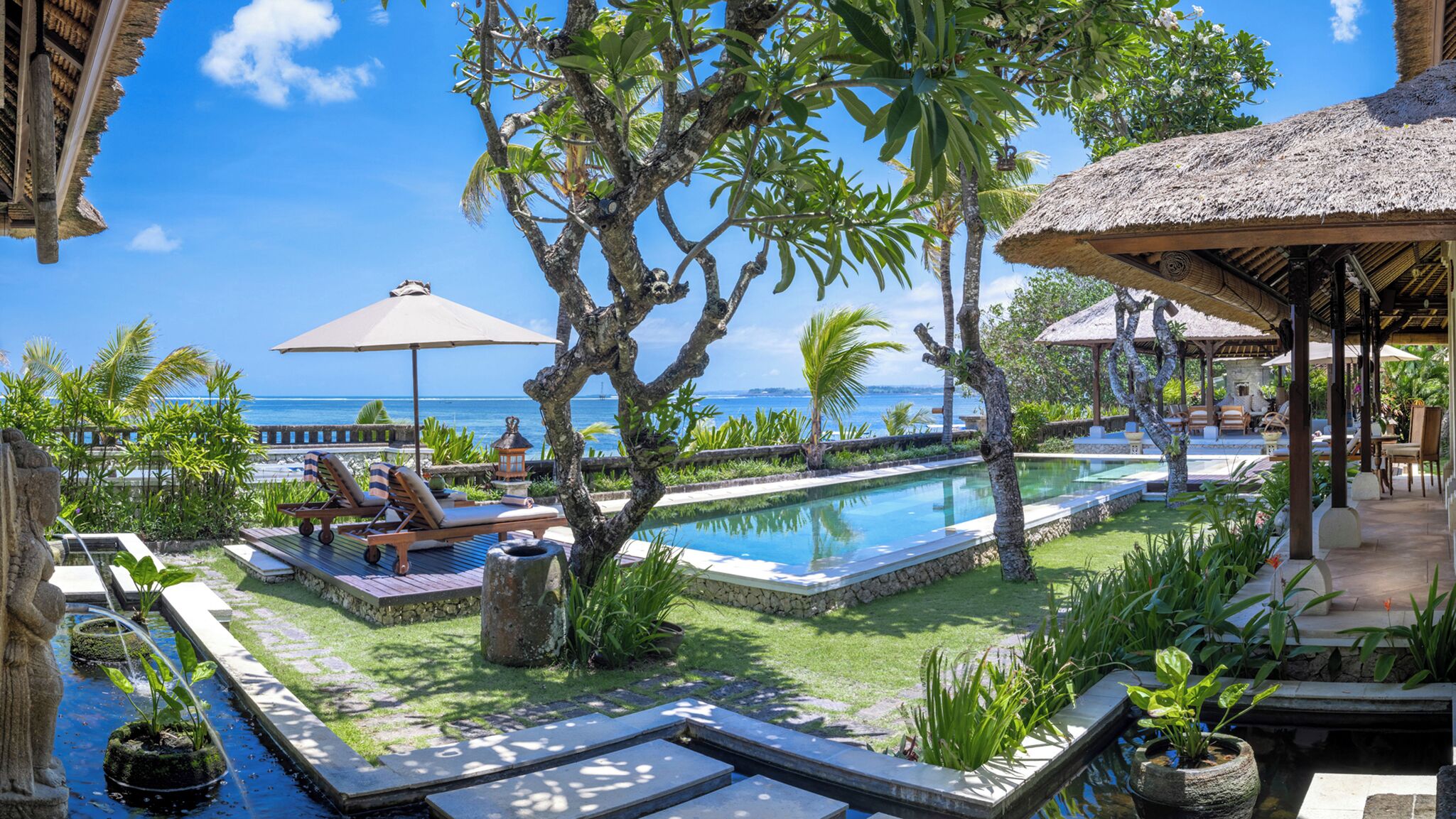 A pool area with lounge chairs, a small pool, and a view of the ocean.
