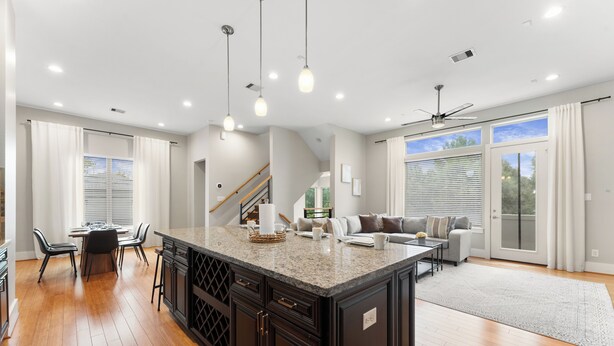 A spacious kitchen with a central island, wooden flooring, and a dining area with chairs and a table. - EaDo Escape • Sleeps 10 - Private Yard & Driveway + Rooftop City Views (Houston)
