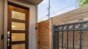 A modern entrance with a wooden door, a metal gate, and a concrete step leading to the door. - EaDo Escape • Sleeps 10 - Private Yard & Driveway + Rooftop City Views (Houston)