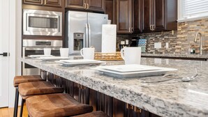 A modern kitchen with dark wood cabinets, stainless steel appliances, and a granite countertop. - EaDo Escape • Sleeps 10 - Private Yard & Driveway + Rooftop City Views (Houston)