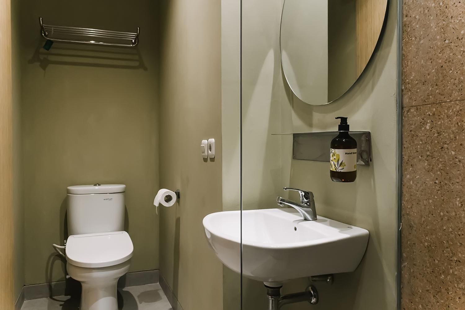 A bathroom with a toilet, a sink, a mirror, and a soap dispenser.