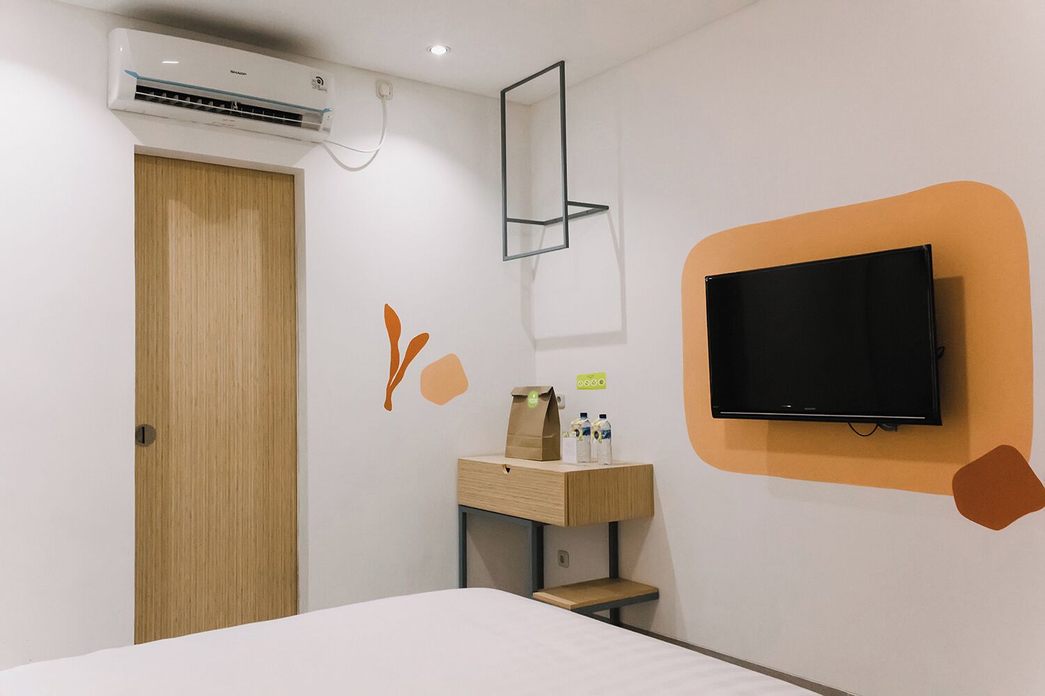 A hotel room with a bed, a TV mounted on the wall, a wooden door, and an air conditioning unit.
