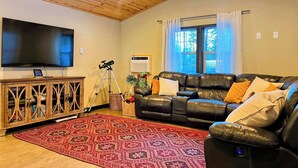 Una sala de estar con un sofá de cuero, un televisor de pantalla plana, un mueble de madera y una alfombra estampada.