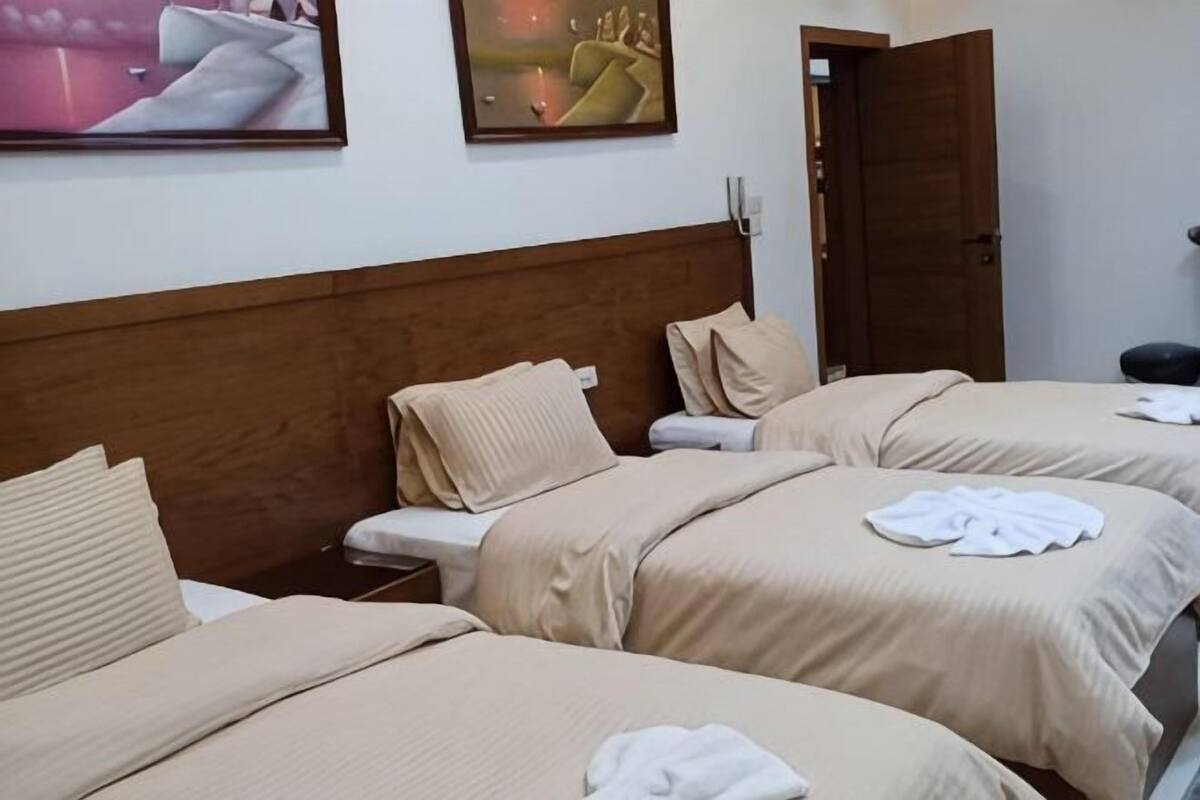 Habitació d'hotel amb tres llits, un panell de capçalera de fusta i una obra d'art a la paret.