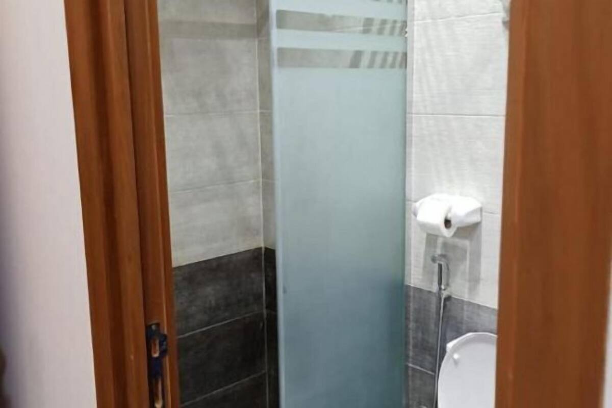 Bany amb dutxa de vidre, vàter i dispensador de tovalloles.