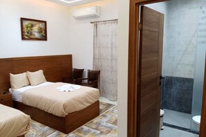 A bedroom with a wooden bed, a bedside table, a chair, a painting on the wall, and a bathroom with a shower and toilet. - New Panorama Inn (Cairo)
