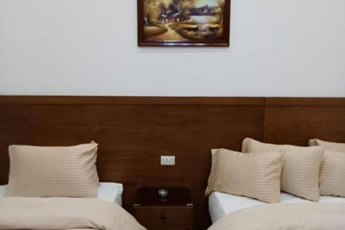 Habitació d'hotel amb dos llits, un panell de fusta al capçal, una tauleta de nit amb una làmpada i un quadre a la paret.
