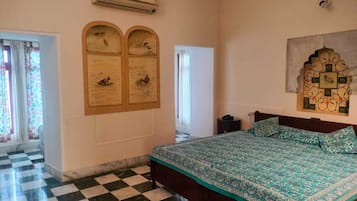 A room with a checkered floor, a bed with a patterned bedspread, a wall-mounted air conditioner, and a decorative wall piece.