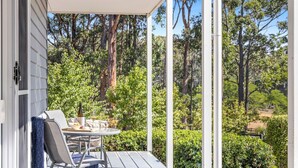A covered outdoor seating area with a table and chairs, overlooking a lush garden and trees. - Forest Edge Daylesford (Eganstown)