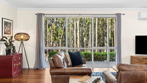 A living room with a large window, a sofa, a coffee table with chess, a floor lamp, and a TV. - Forest Edge Daylesford (Eganstown)