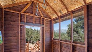 A wooden cabin with a wooden deck, large windows, and a view of a forested landscape.
