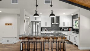 A modern kitchen with a central island, bar stools, stainless steel appliances, and a black ceiling.