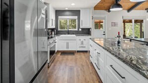 A modern kitchen with white cabinets, a stainless steel refrigerator, and a marble countertop.